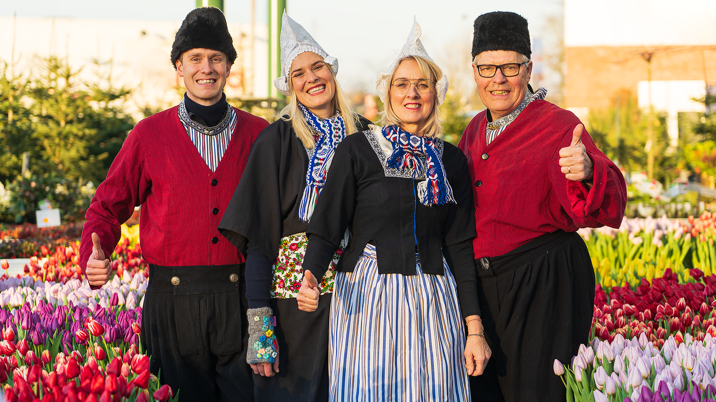 Vier Personen in traditioneller niederländischer Tracht lächeln auf einem bunten Tulpenfeld