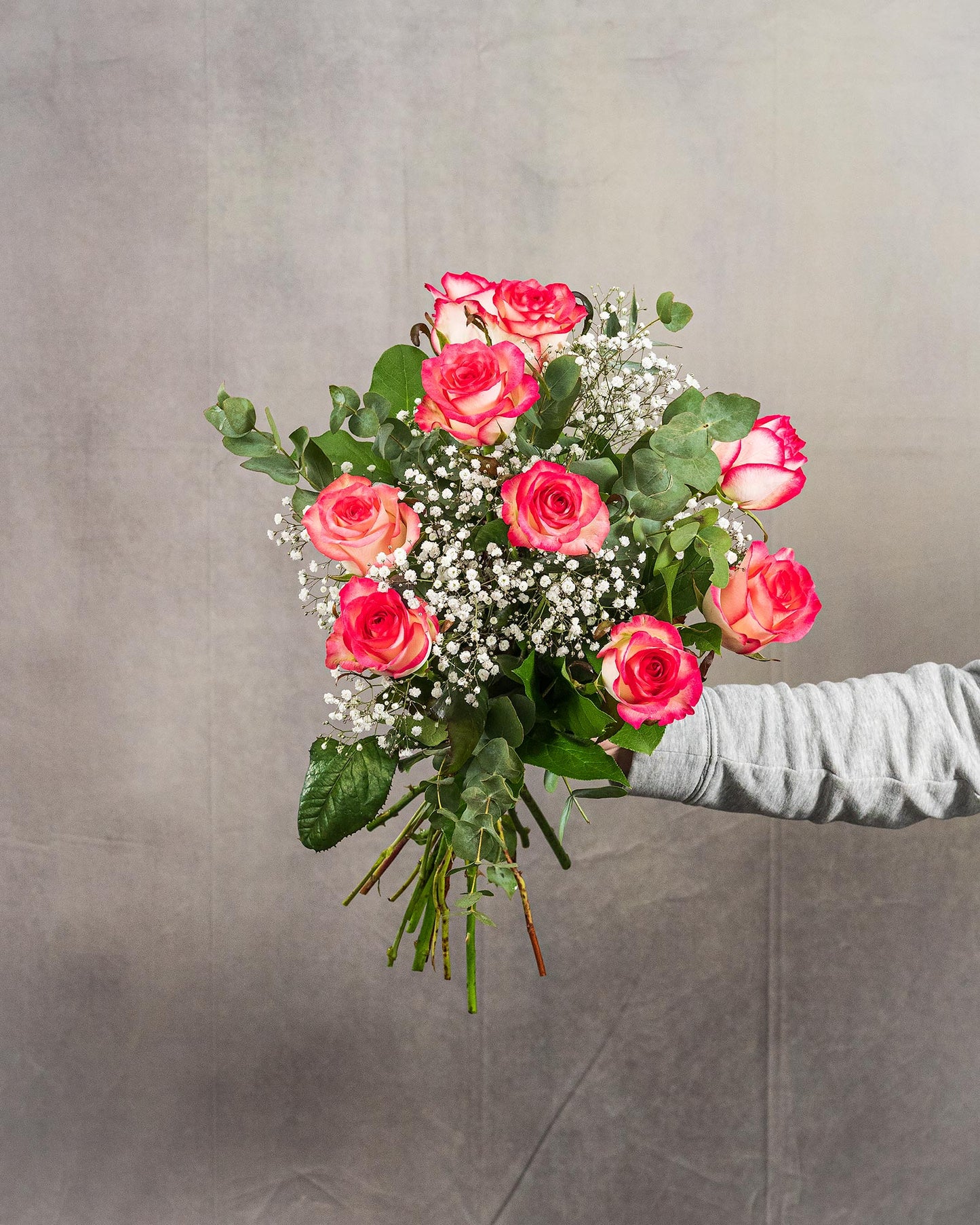 Kleiner Rosenstrauß mit pink-weißen Rosen und Schleierkraut in Hand