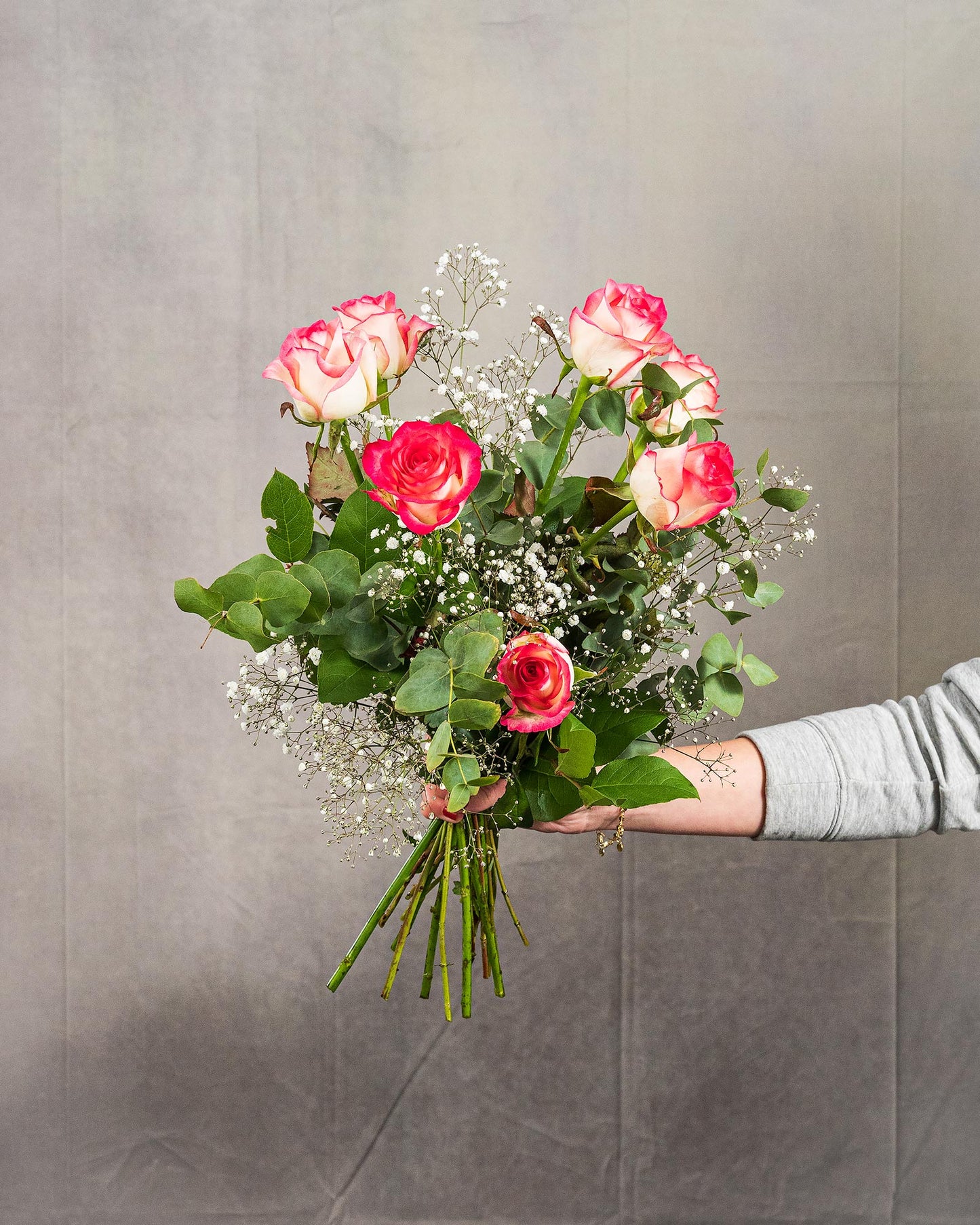 Kleiner Rosenstrauß mit pink-weißen Rosen und Schleierkraut in Hand