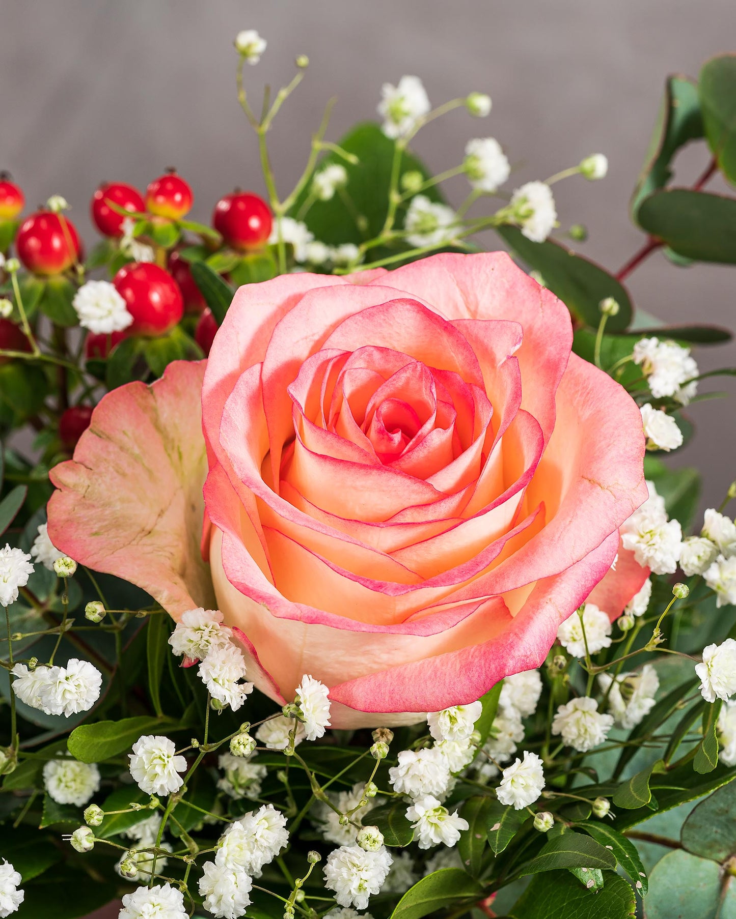 Nahaufnahme einer roséfarbenen Rose mit zarten weißen Schleierkrautblüten und roten Beeren, elegant arrangiert mit Eukalyptusblättern