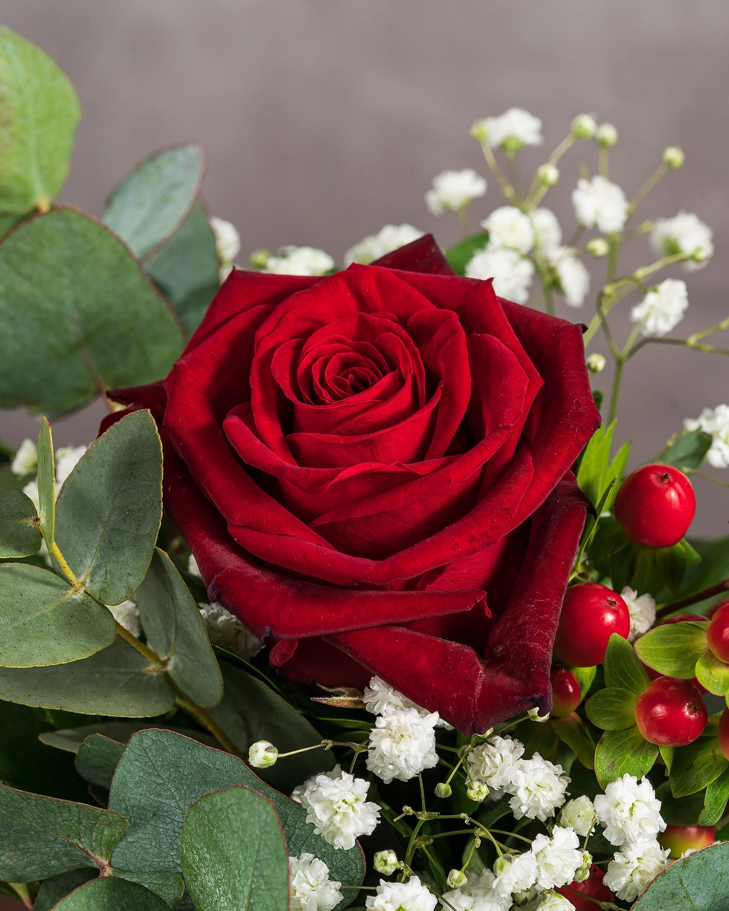 Nahaufnahme einer roten Rose mit Schleierkraut und roten Beeren, umgeben von Eukalyptusblättern